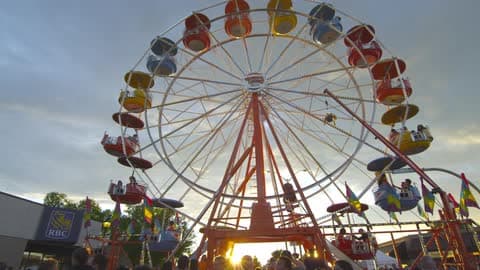 A Ferris Wheel Rotates While A Crowd Passes By