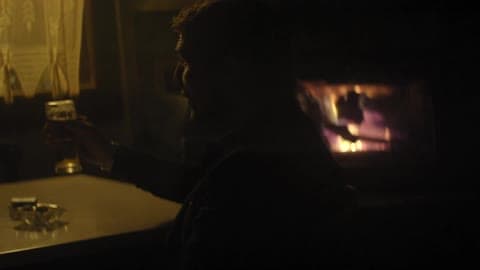 A Man In Black Drinks A Beer In Front Of A Fireplace
