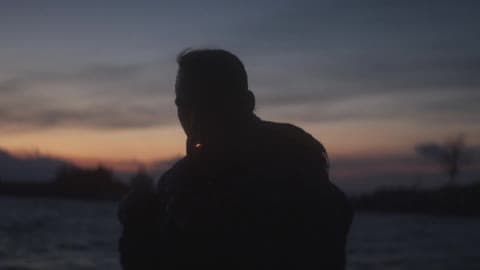 A Man Smokes A Cigarette On A Beach At Dusk