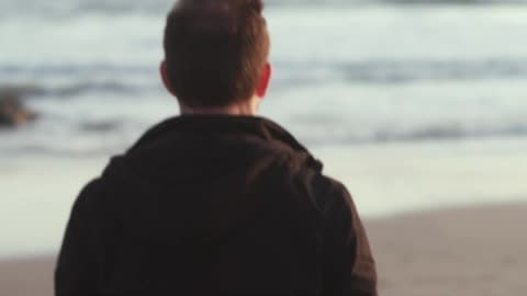 A Man Walking Along A Beach Towards The Water