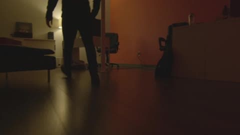 A Man Walking Through A Bedroom, Crouching In Front Of A Cabinet And Opening It