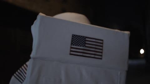 A Person In An American Spacesuit Walks Down An Alley At Night