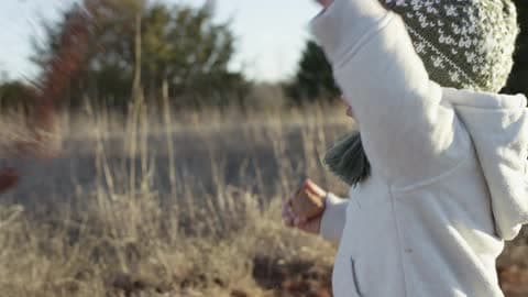 A Toddler Standing In A Field, Holding A Rock In One Hand And Throwing Something With The Other