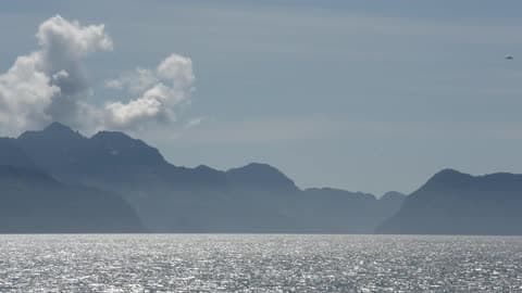 Clouds Hover Over The Mountains While A Body Of Water Flows In The Foreground