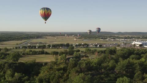 Hot Air Balloons Floating Over Trees, Fields And Homes With Mountain Foothills In The Background