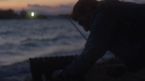 Man Putting Away Fishing Equipment At Sunset