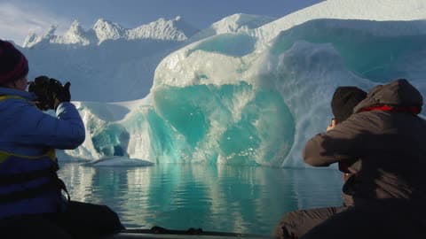 People Taking Photographs Of An Iceberg On A Clear Day
