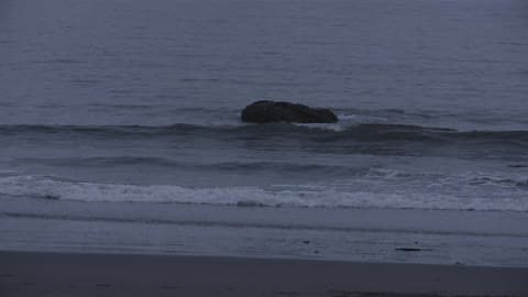 Waves Crashing Around A Rock And Onto A Beach